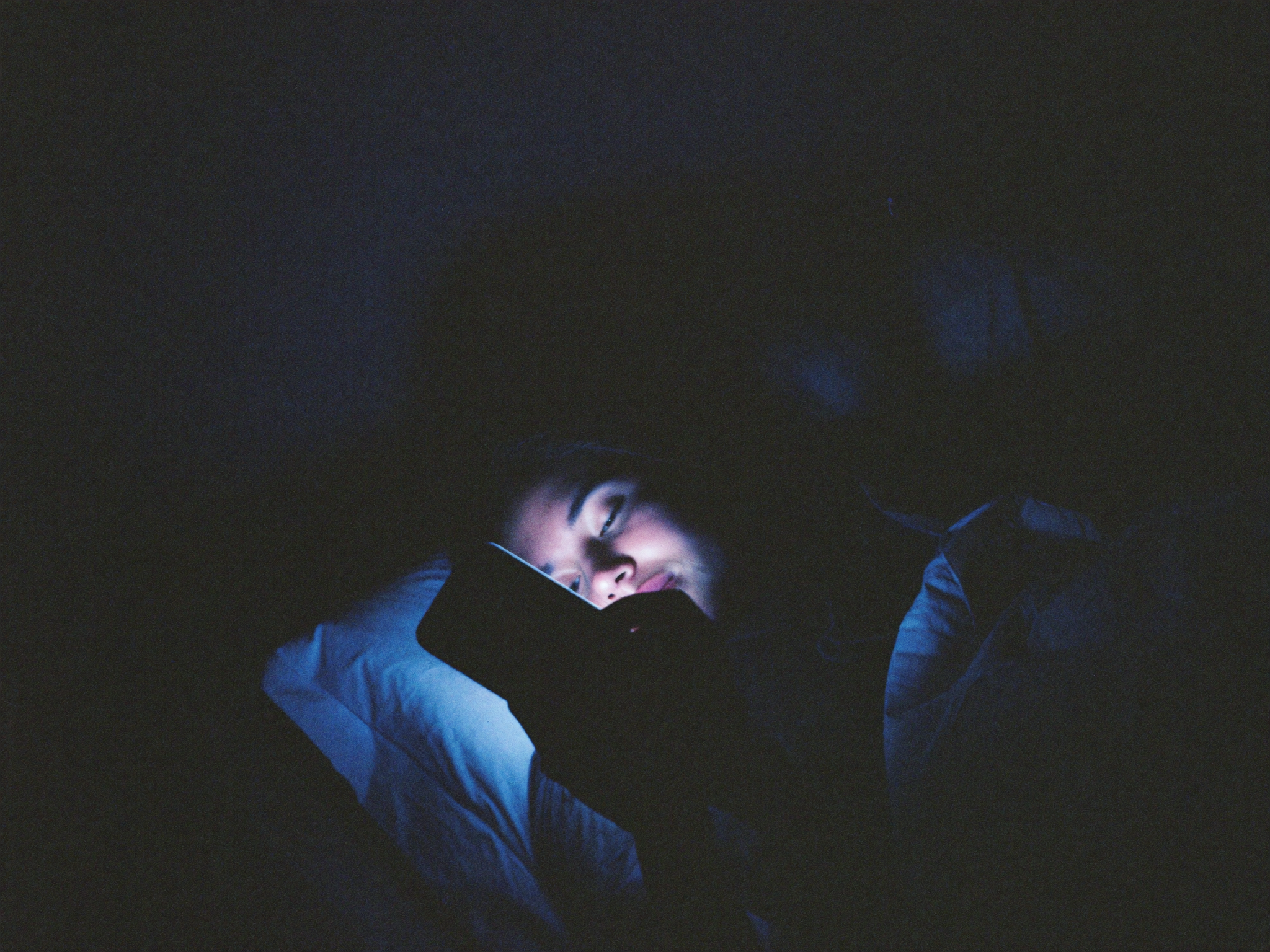 Scrolling in the dark — phone glow on her face